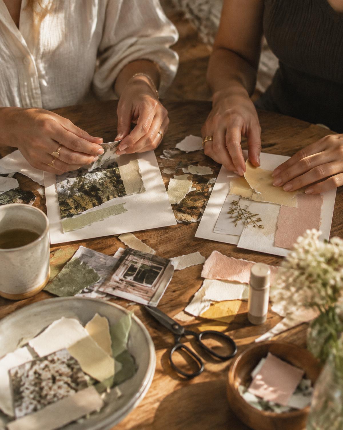 Two women making paper collages together at a wooden table